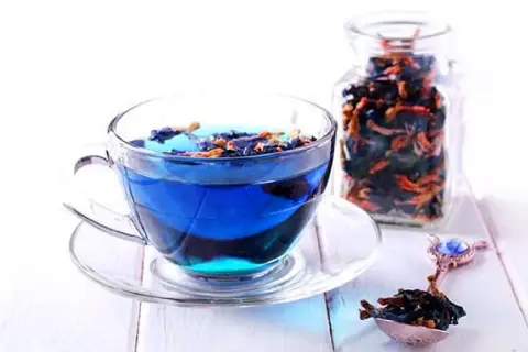 Blauer Tee aus Clitoria ternatea, bekannt für seine Wirkung, in einer Tasse und einem Glasbehälter.