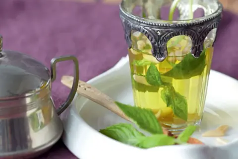 Ein Glas mit Minze ziehen lassen, daneben eine Teekanne.