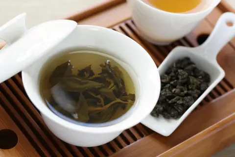 Eine Tasse Oolong Tee, daneben trockene Blätter. Wie viel Oolong Tee am Tag ist gesund?