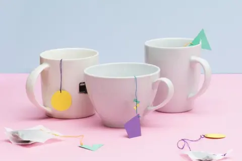 Drei Tassen mit selbstgemachten Teebeuteln, die mit bunten Anhängern verziert sind. Eine schöne Idee, um Teebeutel selber zu machen.