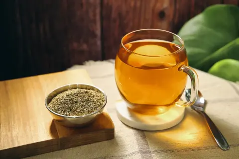 Eine Tasse goldener Thymiantee steht neben einer Schale getrocknetem Thymian. Die beruhigende Thymiantee Wirkung ist spürbar.