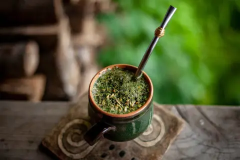 Ein grüner Mate-Becher mit Metallstrohhalm auf einem Holztisch. Informiere dich über mögliche mate tee nebenwirkungen, bevor du ihn genießt.
