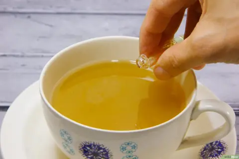 Eine Hand tropft eine Flüssigkeit aus einer kleinen Ampulle in eine Tasse Tee. Die ideale earl grey temperatur wird erreicht.