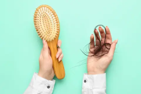 Hände halten Haarbürste und Haarbüschel. Ein Zeichen für Haarausfall, vielleicht nach dem Genuss von schwarzem Tee?