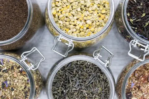 Sechs Gläser mit verschiedenen blattgrad tee Sorten: Kamille, schwarzer Tee, grüner Tee, Rooibos und Kräutermischungen.