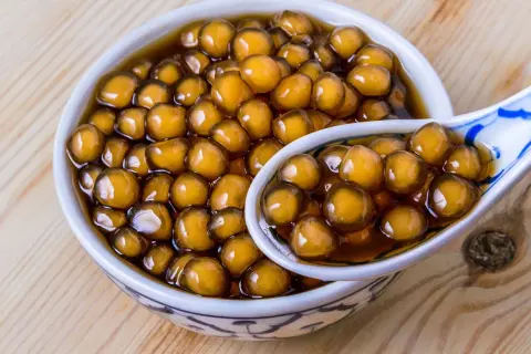 Ein Schälchen mit braunen Tapiokaperlen, perfekt für ein leckeres Boba-Rezept. Eine Löffel voller Perlen zeigt die köstliche Textur.
