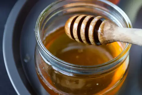 Ein Holzlöffel taucht in ein Glas mit flüssigem Honig. Perfekt zum Süßen von Tee.