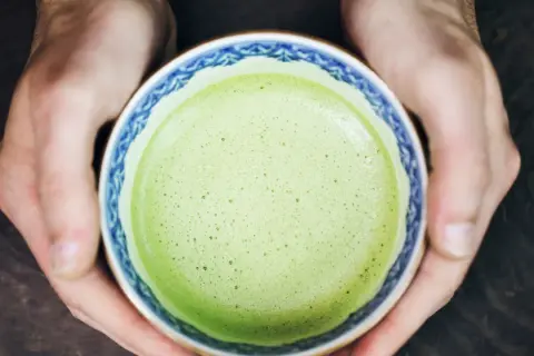 Hände halten eine Schale mit schaumigem, leuchtend grünem Matcha. Für manche ist Matcha ein Genuss, für andere ein Thema bei Histaminintoleranz.