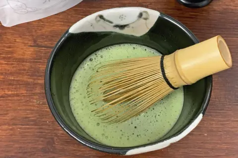 Ein Chasen rührt schaumigen Usucha Matcha in einer Schale.