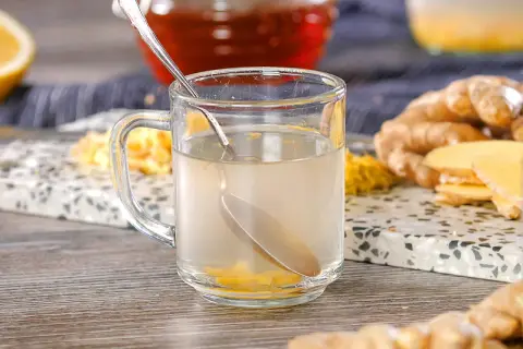 Ein Glas Ingwertee mit frischen Ingwerscheiben und einer Löffel. Die ideale Ziehzeit für Ingwertee ist entscheidend für den Geschmack.