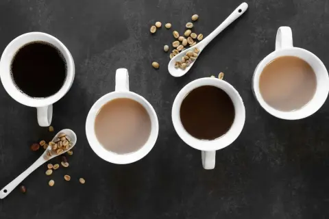 Vier Tassen Kaffee, zwei schwarz, zwei mit Milch, und Löffel mit Kaffeebohnen. Die Entscheidung zwischen Tee vs Kaffee ist hier klar: Kaffee!