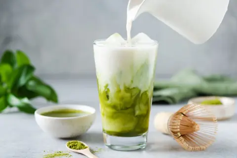 Milch wird in ein Glas mit Eis und Matcha gegossen. Ein einfaches Matcha Latte Rezept für den perfekten Genuss.
