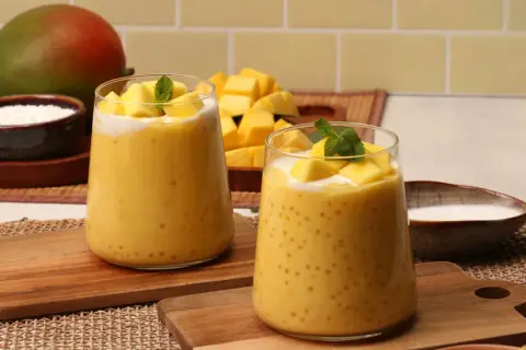Zwei Gläser cremiger Mango-Bubble-Tea mit Tapiokaperlen, garniert mit frischen Mangostücken und Minze. Ein Mango-Rezept zum Genießen.