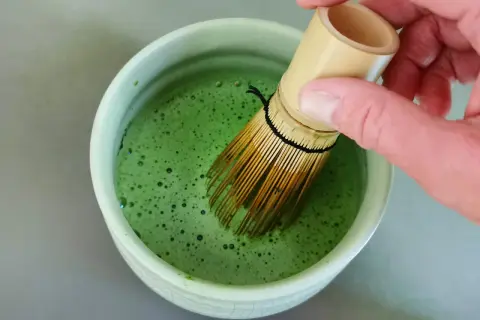 Hand whisking bright green matcha in a bowl. The ideal matcha temperatur is crucial for a smooth, frothy brew.