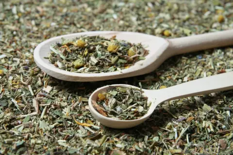 Zwei Holzlöffel gefüllt mit Kräutern für Tee selber machen Rezepte. Die Mischung duftet nach Kamille und anderen Heilkräutern.