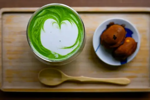 Ein Glas cremiger Matcha mit Herz-Latté-Art und zwei süßen Leckereien. Perfekt zum Matcha trinken.