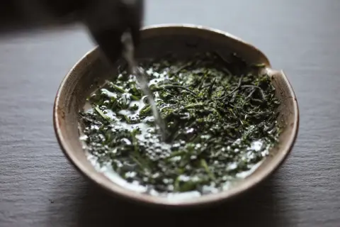 Wasser fließt in eine Schale mit grünen Teeblättern für die Gyokuro Zubereitung.