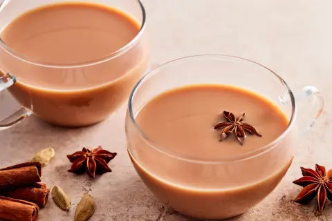 Zwei Tassen cremiger Chai Latte, garniert mit Sternanis. Zimtstangen und Kardamomkapseln deuten auf ein authentisches indischer chai rezept hin.