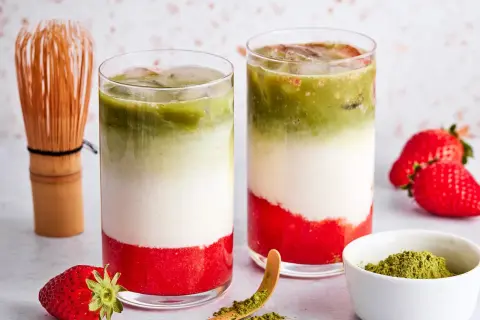 Zwei Schichten-Getränke mit Erdbeerpüree, Milch und Matcha. Ein Chasen und frische Erdbeeren deuten an, was ist eigentlich in rotem Matcha drin.