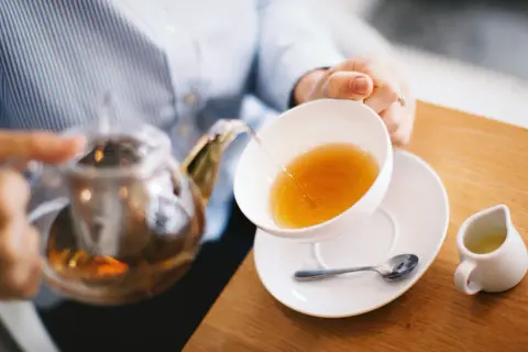 Frau gießt Tee ein. Welcher Tee verbrennt Fett? Grüner Tee ist bekannt dafür, den Stoffwechsel anzukurbeln.