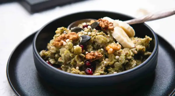 Grüner, cremiger matcha porridge mit Nüssen, Kernen, Granatapfel und Bananenscheiben. Ein gesundes Frühstück.
