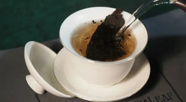 Heißes Wasser fließt in eine Teetasse mit Pu-erh Tee. Mögliche Pu-erh Tee Nebenwirkungen sind selten, aber bei übermäßigem Genuss zu beachten.