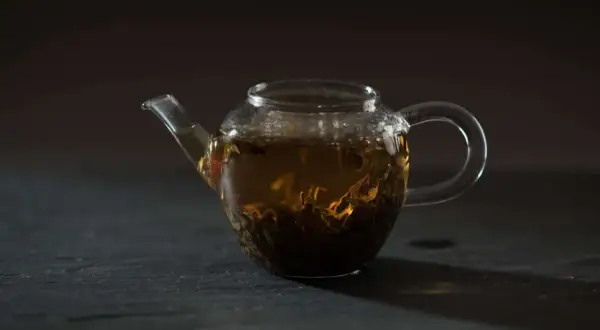 Glas-Teekanne mit braunem Tee und sichtbaren Tee-Inhaltsstoffen.