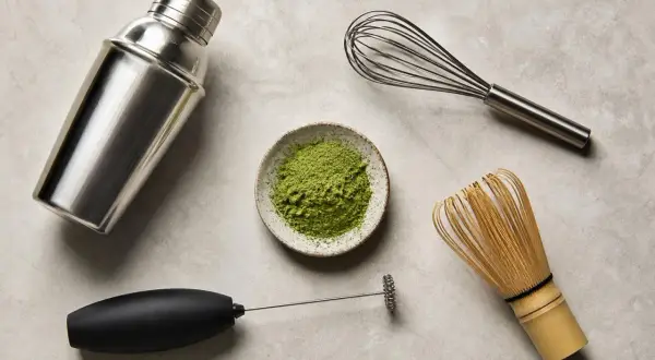 Matcha-Zubereitung: Pulver in Schale, daneben ein Milchaufschäumer, ein Schneebesen und ein Shaker. So gelingt Matcha ohne besen.