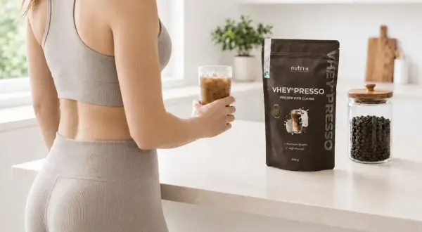 Frau hält Eiskaffee, neben VHEY® PRESSO Protein-Pulver. Die Koffein-Wirkdauer wird durch den belebenden Drink unterstützt.