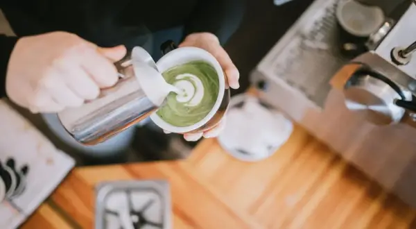 Barista verziert grünen Matcha-Tee mit Milchschaum. Perfekt für den Start in den Tag, auch auf leeren Magen.