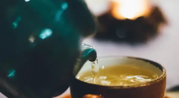Ein grüner Teekrug gießt goldenen Tee in eine orangefarbene Tasse. Welcher Tee treibt nicht? Dieser hier, der Ruhe und Wärme verspricht.