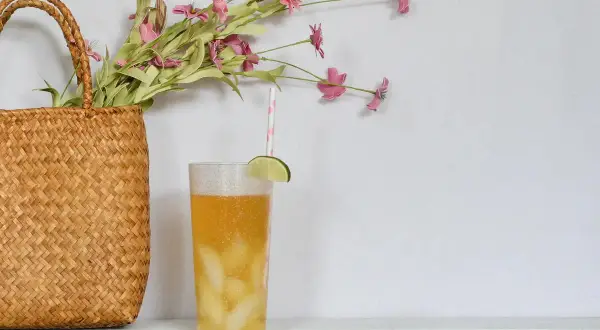 Erfrischender Drink mit Limette und Eis, daneben ein Korb mit Blumen. Perfekt, um Minztee selber zu machen und den Sommer zu genießen.