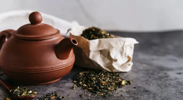 Braune Teekanne mit losem Tee und einem Löffel, bereit für den Aufguss Tee.
