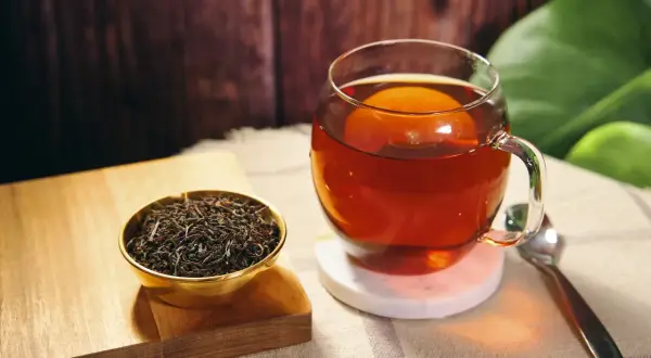 Eine Tasse heißer Ceylon Tee, reich an Koffein, neben einer Schale trockener Teeblätter.