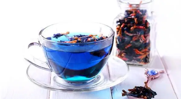 Blauer Tee aus Clitoria ternatea, bekannt für seine Wirkung, in einer Tasse und einem Glasbehälter.