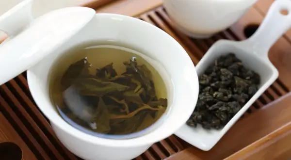 Eine Tasse Oolong Tee, daneben trockene Blätter. Wie viel Oolong Tee am Tag ist gesund?