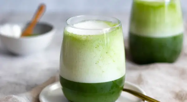 Zwei Gläser mit geschichtetem Matcha-Latte, die die perfekte Matcha-Zubereitung zeigen. Ein Löffel liegt daneben.