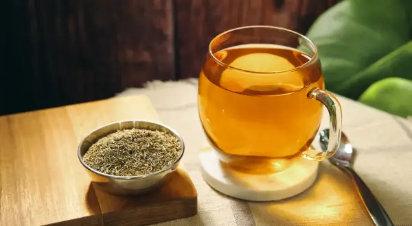 Eine Tasse goldener Thymiantee steht neben einer Schale getrocknetem Thymian. Die beruhigende Thymiantee Wirkung ist spürbar.