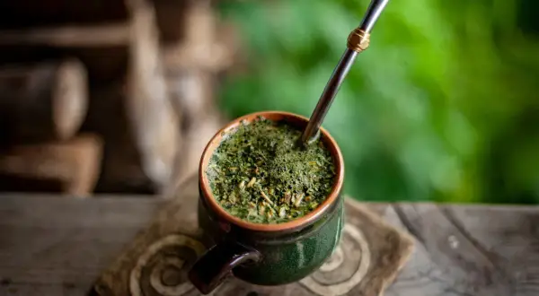 Ein grüner Mate-Becher mit Metallstrohhalm auf einem Holztisch. Informiere dich über mögliche mate tee nebenwirkungen, bevor du ihn genießt.