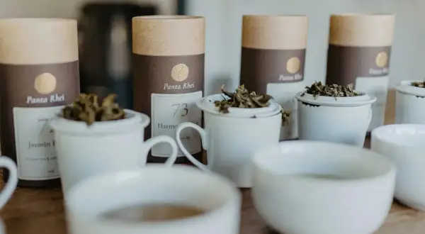 Bereit für den perfekten tee am morgen? Mehrere weiße Teetassen mit losem Tee und braune Röhren mit Teelabeln stehen bereit.