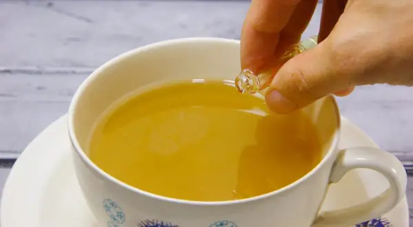 Eine Hand tropft eine Flüssigkeit aus einer kleinen Ampulle in eine Tasse Tee. Die ideale earl grey temperatur wird erreicht.