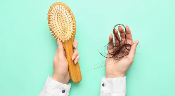 Hände halten Haarbürste und Haarbüschel. Ein Zeichen für Haarausfall, vielleicht nach dem Genuss von schwarzem Tee?