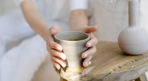 Sanfte Hände halten eine Tasse Tee. Ein Moment der Ruhe, perfekt, um abends Brennnesseltee zu trinken.