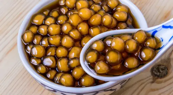 Ein Schälchen mit braunen Tapiokaperlen, perfekt für ein leckeres Boba-Rezept. Eine Löffel voller Perlen zeigt die köstliche Textur.
