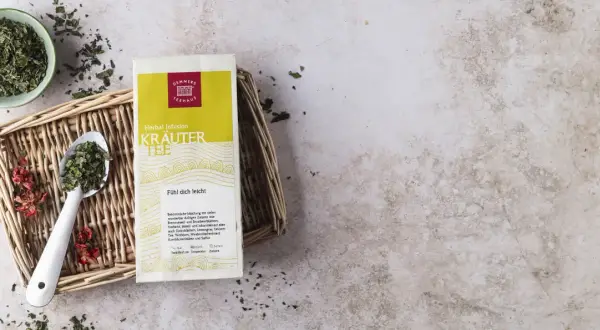 Kräutertee-Packung mit Löffel und Schale voller Kräuter. Die tee temperatur tabelle gibt Hinweise zur Zubereitung.