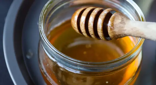 Ein Holzlöffel taucht in ein Glas mit flüssigem Honig. Perfekt zum Süßen von Tee.