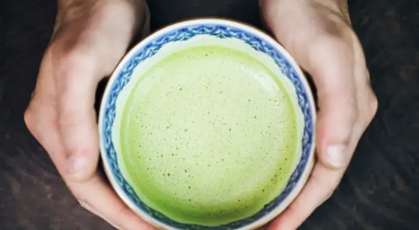 Hände halten eine Schale mit schaumigem, leuchtend grünem Matcha. Für manche ist Matcha ein Genuss, für andere ein Thema bei Histaminintoleranz.