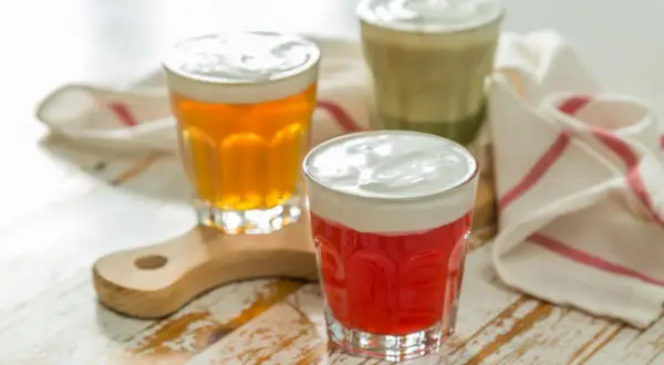 Drei Gläser mit bunten Getränken und cremiger Käseschaumhaube. Ein rotes, ein bernsteinfarbenes und ein grünes Cheese Tea.