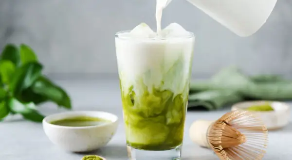 Milch wird in ein Glas mit Eis und Matcha gegossen. Ein einfaches Matcha Latte Rezept für den perfekten Genuss.