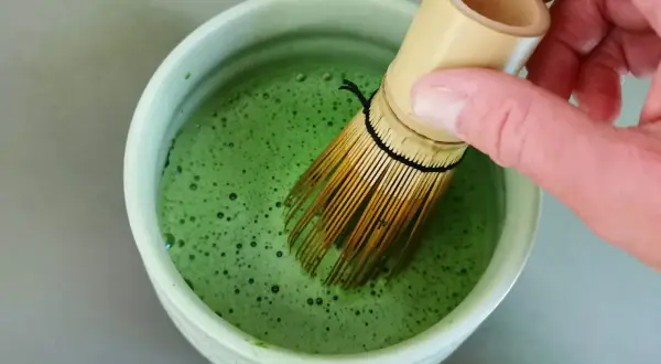 Hand whisking bright green matcha in a bowl. The ideal matcha temperatur is crucial for a smooth, frothy brew.